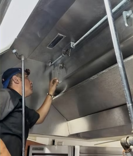 Certified service technician inspecting a clean kitchen exhaust hood
